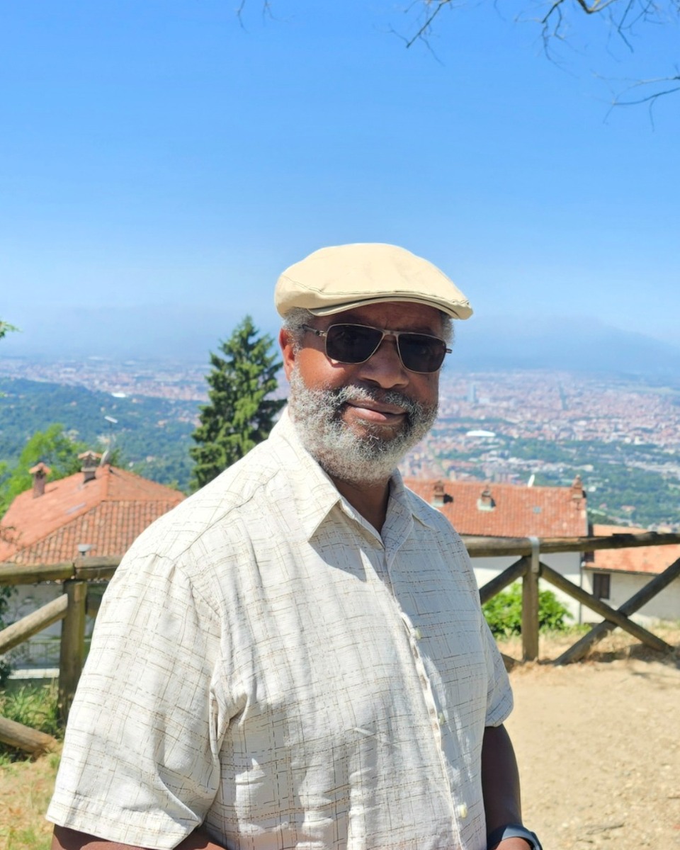 Fred Johnson standing outdoors in Turin, Italy, with the city and mountains behind him
